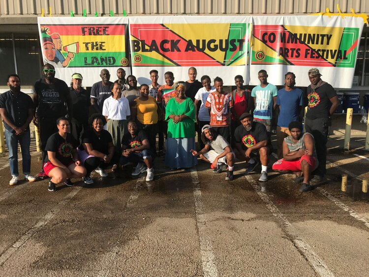 Group of people standing in front of a banner reading, "Free the land. Black August. Community Arts Festival"