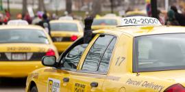 Line of Union Cabs at a protest. A driver is holding a raised fist out of their window.