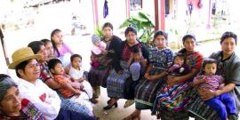 Mayan women and their children sit and listen to a presentation.
