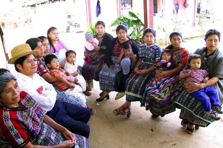 Mayan women and their children sit and listen to a presentation.