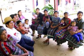 Mayan women and their children sit and listen to a presentation.