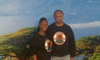 Elders and cofounders Tamu (left) and Hekuma Kanyama standing in front of a Mt. Kilimanjaro mural on the walls of Café ULU.